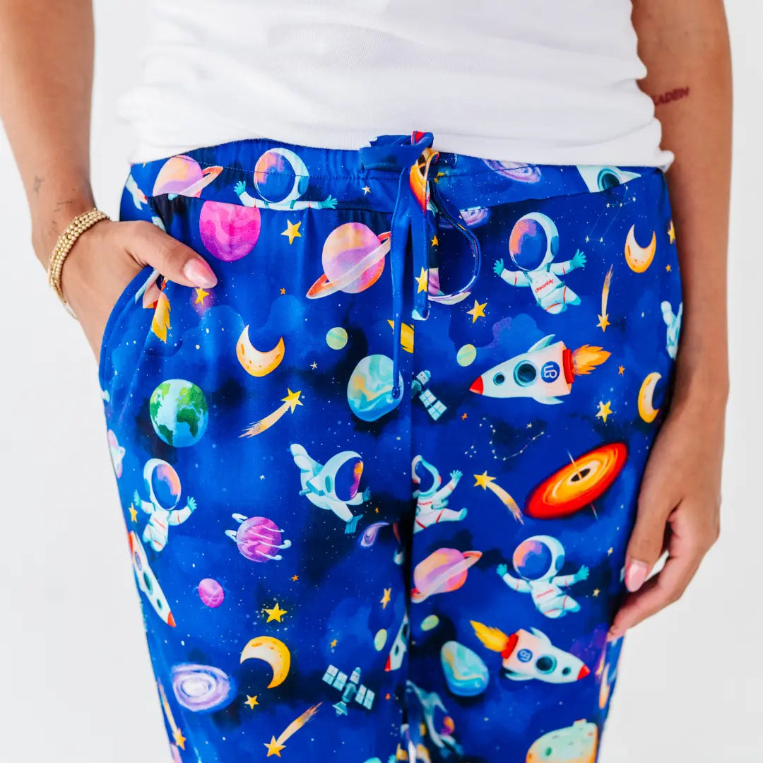 Close-up of royal blue drawstring pajama pants printed with astronauts, planets, rockets, and moons, worn with a white tee.